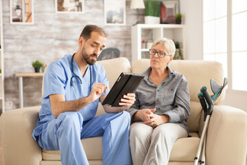 Doctor in nursing home using tablet computer while taking with female pensioner.
