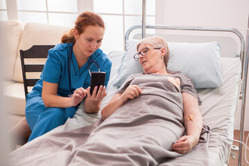 Female doctor helping senior woman in nursing home to use her phone.