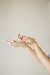 Gentle hands are folded together and held palms up. There are moles on the hands. The background of the image is plain and light brown. High quality photo