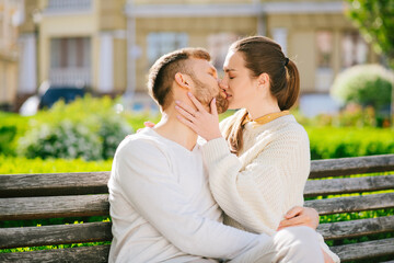 Naklejka premium Young man and woman kissing on bench in city park.