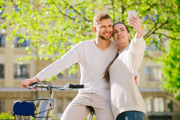 Happy man on bicycle and woman with smartphone in outstretched hand.