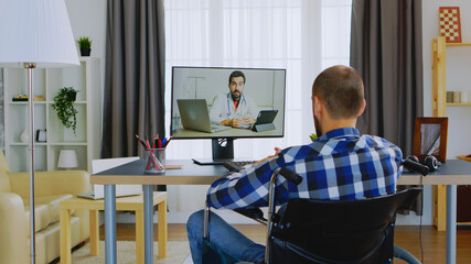 Man with walking disability in wheelchair talking with his doctor on video call.