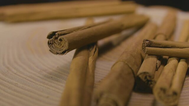 Ceylon cinnamon sticks falling into frame on wooden platform. Close up. slow motion.