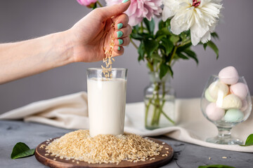 Hand is pouring rice grains into a glass of natural rice milk. Alternative vegetarian drink for a healthy diet