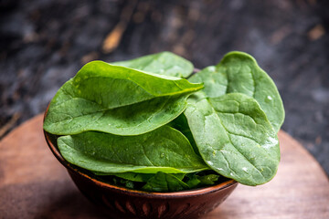 Leaves of fresh spinach in a plate on a dark background. Healthy vegetarian food
