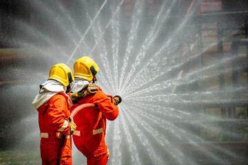 Two brave firefighter in fire suit on rescue duty using water from hose extinguishing fighting with...