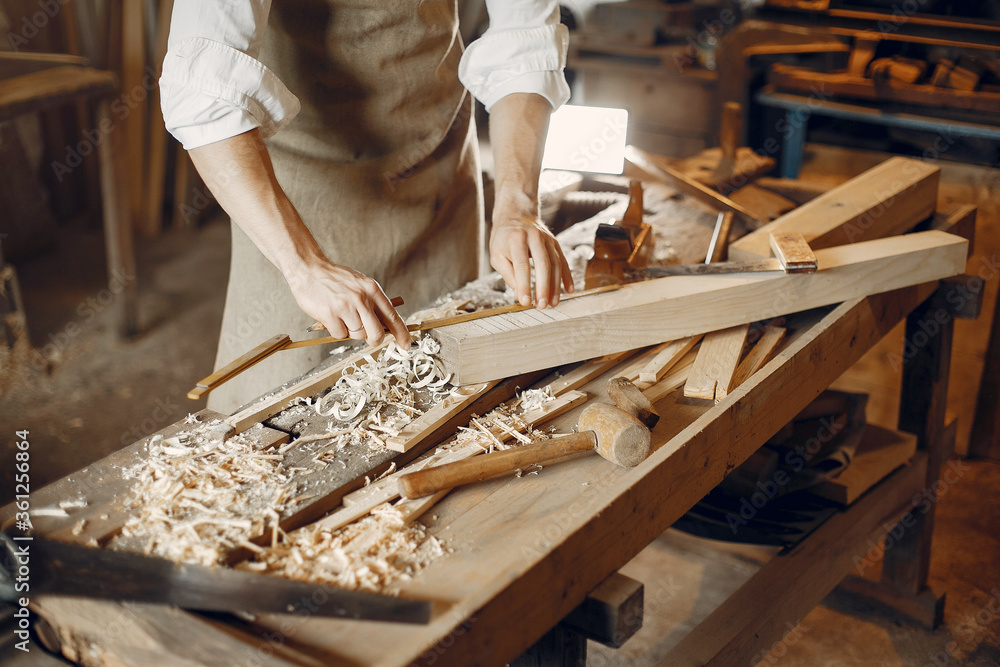 Wall mural Man working with a wood. Carpenter in a white shirt. Worker measures a board