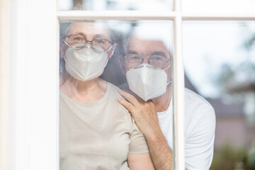 Elderly couple wearing protective face masks watch through their home window during the coronavirus epidemic