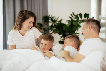 Obraz premium Young family enjoying in bed. Happy parents with sons relaxing in bed. 