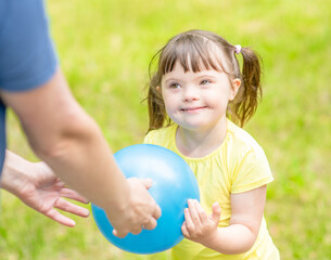 Little girl with syndrome down and her mother play with a ball in a summer park