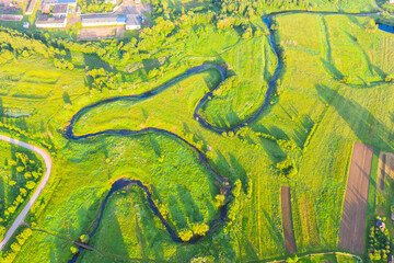 Top aerial view of the natural rural landscape valley of a meandering river among green fields and forests.