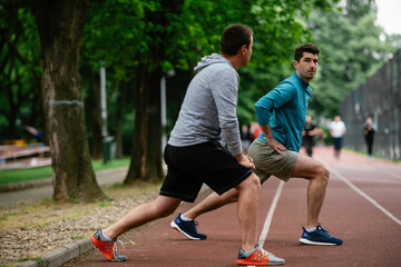 Young men exercising on a race track. Two young friends training outdoors.	