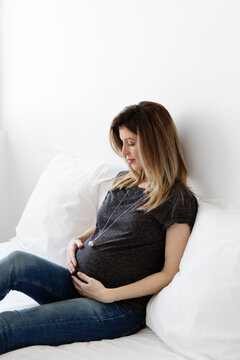 Pregnant woman sitting on bed looking at her bola necklace
