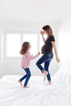 Pregnant woman and her little girl dancing together on the bed