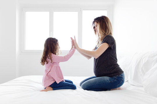 Pregnant mother and her little girl playing together and clapping hands