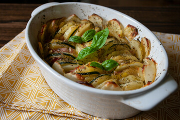 Casserole dish recipe.Hearty potato gratin bacon and zucchini,freshly served from the oven on a wooden table. Close up.