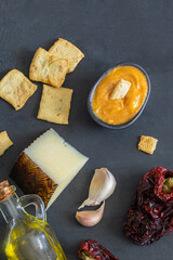 Top view of  Almogrote (La Gomera Island cheese paste ) black bowl with ingredients hard goat cheese, peppers, olive oil and garlic on light concrete background.