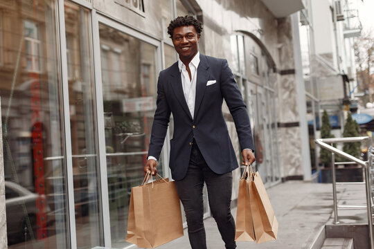 Black man in a city. Guy with shopping bags. Man in a black suit;