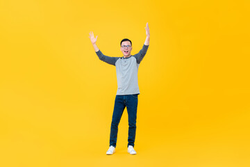 Fototapeta na wymiar Full body portrait of cheerful young Asian man raising both arms in the air isolated on yellow background