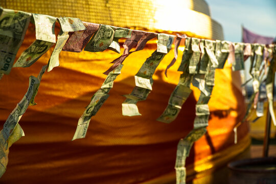 aht banknotes flutter on string against wrapped stupa, offering at Buddhist monastery.
