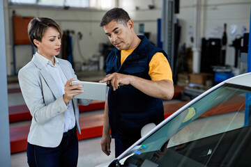 Businesswoman and car repairman using digital tablet in a workshop.