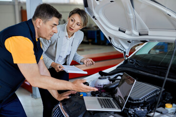 Businesswoman and auto repairman using laptop while testing car's performance in a workshop.