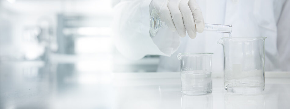 scientist in white coat poring water into glass beaker in medical laboratory science background