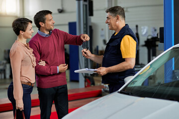 Happy couple giving car key to their auto repairman in a workshop.