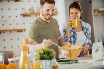 Young couple making pancakes together at home. Loving couple having fun while cooking.	