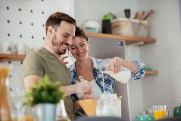 Young couple making pancakes together at home. Loving couple having fun while cooking.	