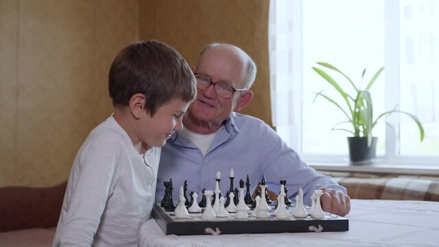 elderly men with a male child play educational board games, grandfather and grandson play chess at a table indoors