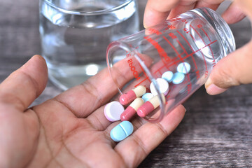 Pills on woman' s hand with glass medicine and glass of water background