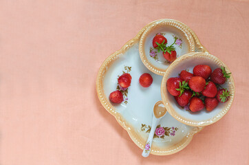 Obraz na płótnie Canvas ripe red strawberries in porcelain plates on a tray on a coral background