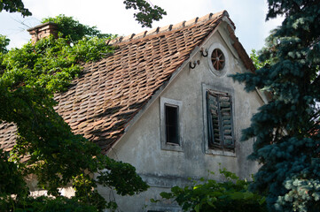Fototapeta na wymiar Attic tiled roof of an old house, window with shutters. Slovenia.