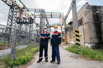 Engineers electrical substations conduct a survey of modern high-voltage equipment in the mask at the time of pandemia. Energy. Industry