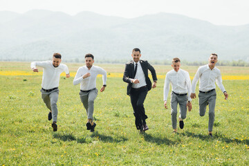 Groomsmen and groom posing outdoors on the wedding day. Funny wedding moment for best groom friends. Man hug each other