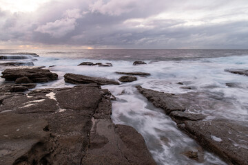 Rock formation on the coastline with water flowing on them,