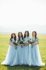 Fototapeta na wymiar attractive gentle bridesmaids standing in nice dresses and with bouquets in hands and having fun