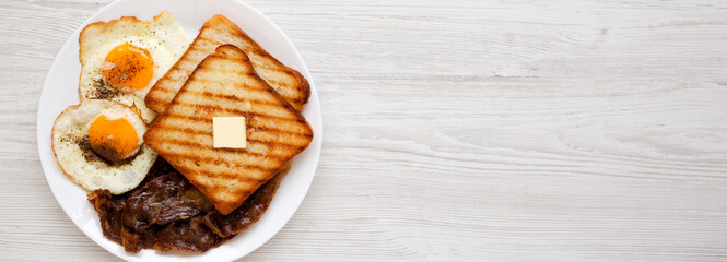 Homemade Healthy Sunnyside Eggs Breakfast on a white plate on a white wooden background, top view. Flat lay, overhead, from above. Space for text.