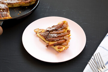 Homemade Apple Dutch Pannekoek Pancake on a pink plate on a black background, side view.