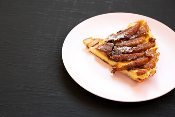 Homemade Apple Dutch Pannekoek Pancake on a pink plate on a black surface, side view. Copy space.