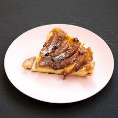 Homemade Apple Dutch Pannekoek Pancake on a pink plate on a black background, side view. Close-up.