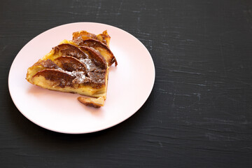 Homemade Apple Dutch Pannekoek Pancake on a pink plate on a black surface, side view. Space for text.