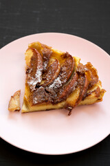 Homemade Apple Dutch Pannekoek Pancake on a pink plate on a black background, side view. Close-up.