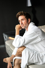 Young, handsome man in the morning thinking while sitting in a hotel room in a robe