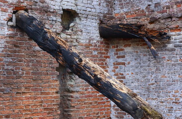 An old brick wall with a rotten burnt wooden beam