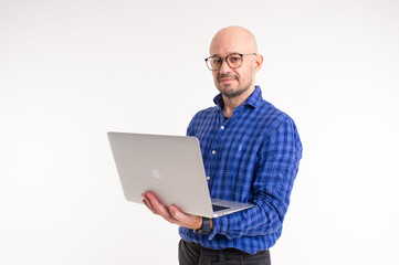 Handsome caucasian man without hair in blue shirt, black trousers and blue socks do freelance with laptop isolated on white background