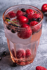 Fresh cold sparkling water drink with cherry, raspberry and currant berries in red faceted glass on stone concrete background, summer diet beverage, angle view macro
