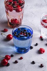 Fresh cold sparkling water drink with cherry, raspberry and currant berries in three colorful glass on stone concrete background, summer diet beverage, angle view