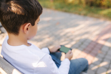 Teenage boy play online games on his smartphone in the park after lessons in school